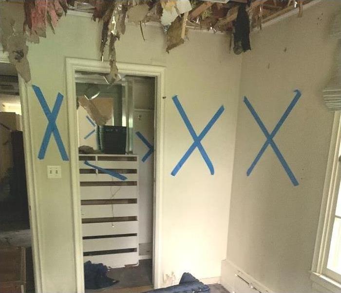 An Albany home with the ceiling broken and insulation exposed and the walls marked with X's in tape.