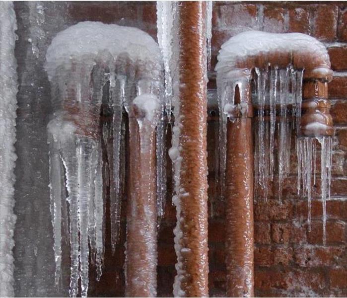 Pipes against a brick wall covered with ice and icicles hanging from them.